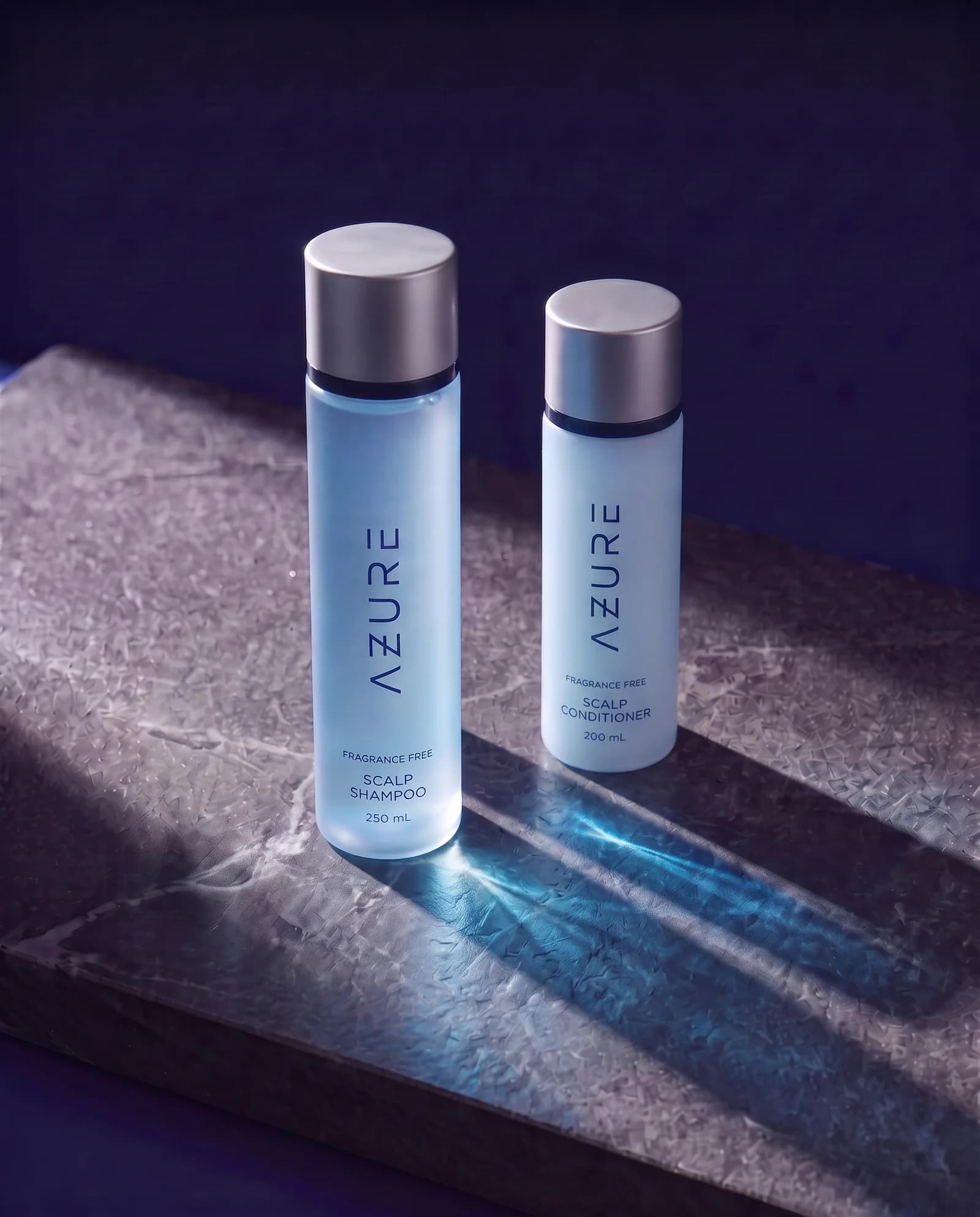 AZURE Scalp Shampoo and the smaller Scalp Conditioner standing on dark stone, in raking light